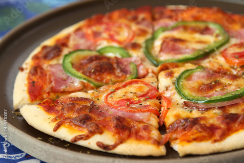 Italian pizza with ham  mozzarella cheese  tomato and bell pepper on ceramic plate.