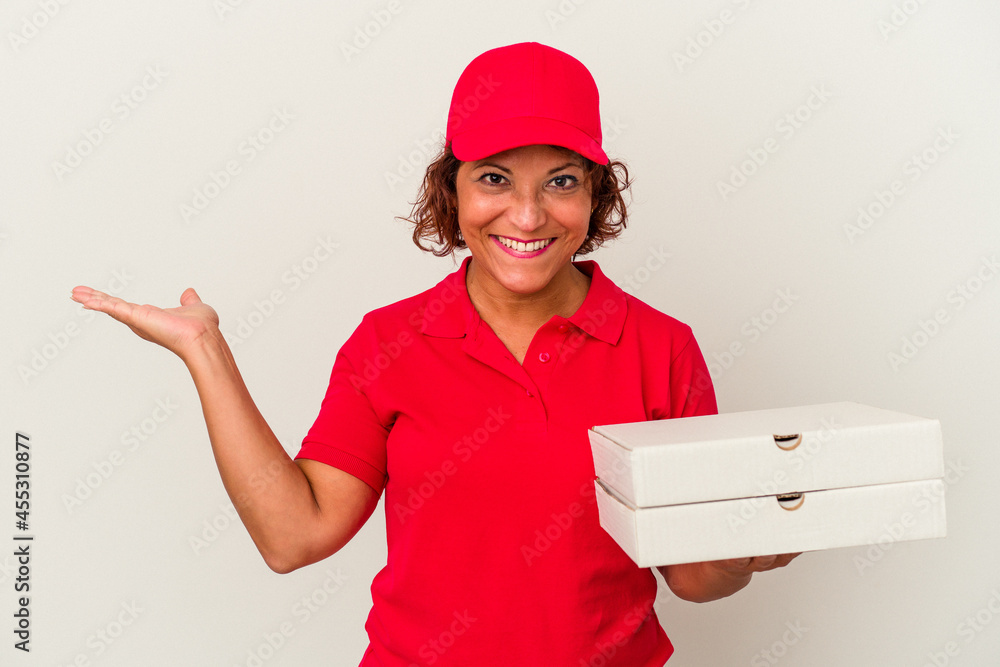 Middle age delivery woman taking pizzas isolated on white background showing a copy space on a palm and holding another hand on waist. Middle age delivery woman taking pizzas isolated on white background showing a copy space on a palm and holding another hand on waist.