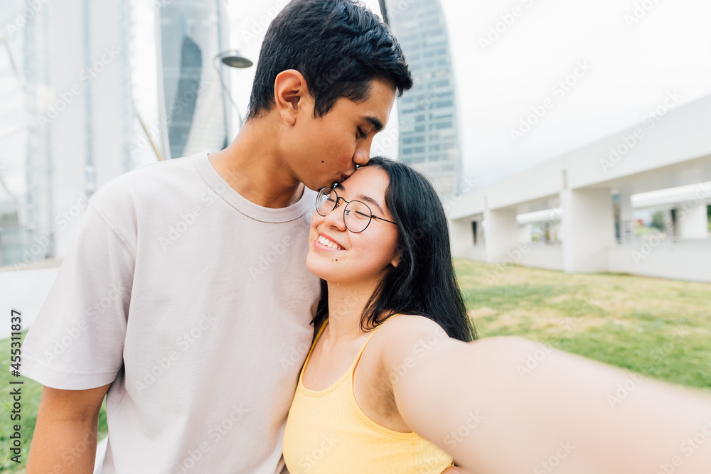 Obraz premium Young asian couple in love outdoors taking selfie kissing forehead smiling happy