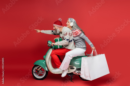 Photography cheerful middle aged asian woman holding shopping bags while riding moped with h