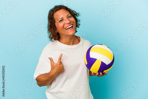 Middle age latin woman playing volleyball isolated on blue background pointing with finger at you as if inviting come closer.