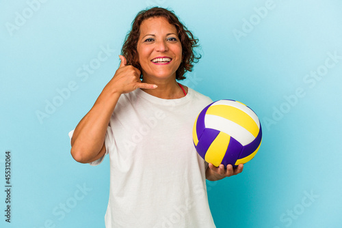 Middle age latin woman playing volleyball isolated on blue background showing a mobile phone call gesture with fingers.