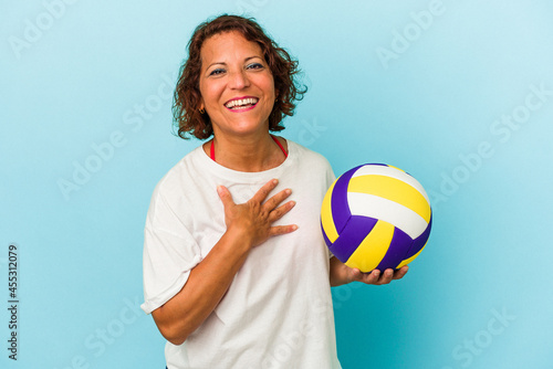 Middle age latin woman playing volleyball isolated on blue background laughs out loudly keeping hand on chest.