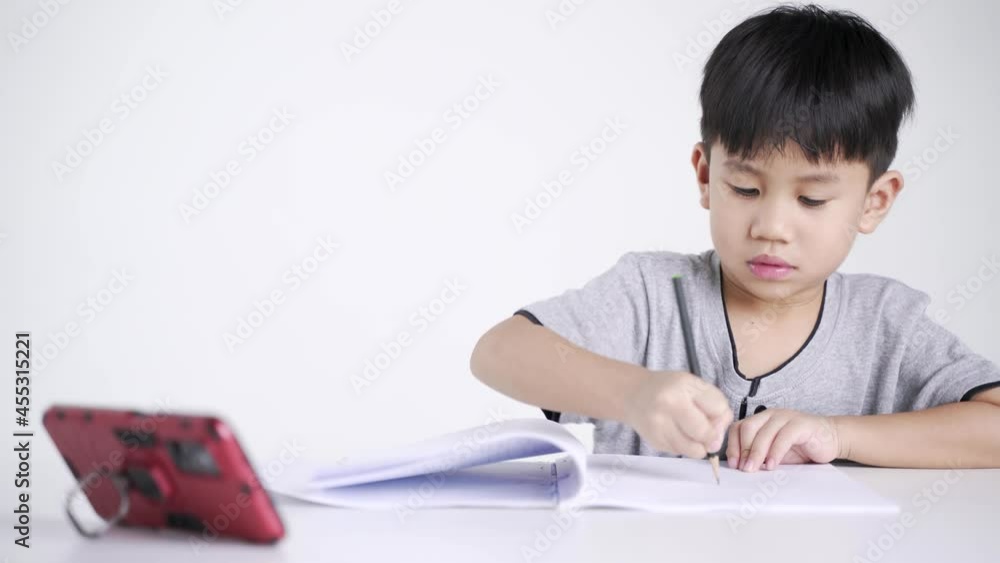 Asian boy about 5 years old writing while watching a mobile phone as studying online due to Covid 19 pandemic Asian boy about 5 years old writing while watching a mobile phone as studying online due to Covid 19 pandemic