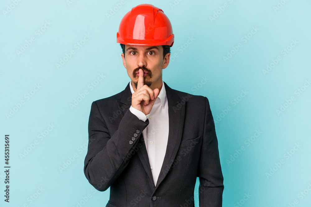Young architect caucasian man isolated on blue background keeping a secret or asking for silence. Young architect caucasian man isolated on blue background keeping a secret or asking for silence.