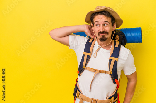 Young caucasian hiker man isolated on yellow background touching back of head, thinking and making a choice.