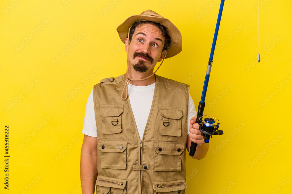 Young caucasian fisherman holding rod isolated on yellow background dreaming of achieving goals and purposes Young caucasian fisherman holding rod isolated on yellow background dreaming of achieving goals and purposes