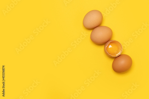 Raw brown chicken eggs and one broken egg with yolk on yellow background