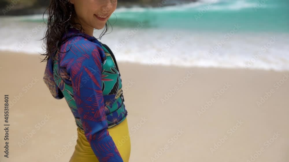 Axel Closeup portrait of beautiful young woman standing on tropical beach. Camera following her body and girl smiling playfully. Woman posing with sand all over her in front of beach and azure sea