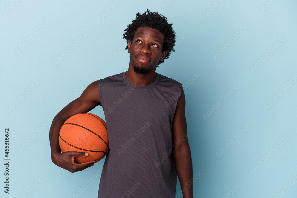 Young african american man playing basketball isolated on blue background dreaming of achieving goals and purposes Young african american man playing basketball isolated on blue background dreaming of achieving goals and purposes
