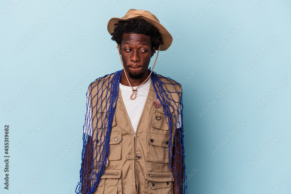 Young african american fisherman holding a net isolated on blue background confused, feels doubtful and unsure. Young african american fisherman holding a net isolated on blue background confused, feels doubtful and unsure.