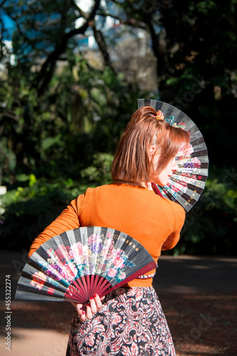 woman with fans posing in a park with flowers