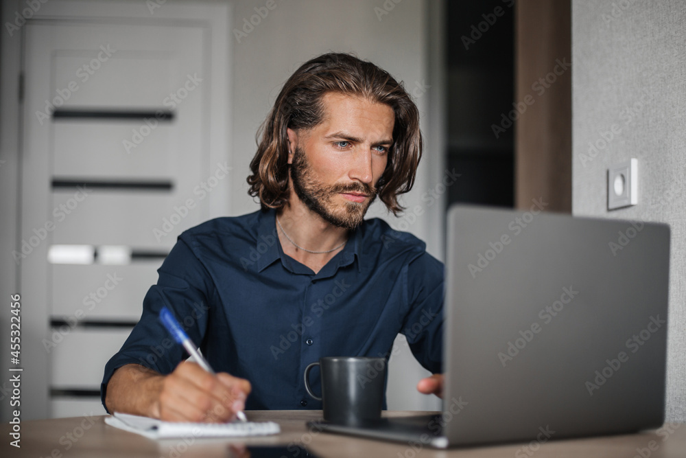 Concentrated middle aged man working on laptop and writing in notepad Concentrated middle aged man working on laptop and writing in notepad