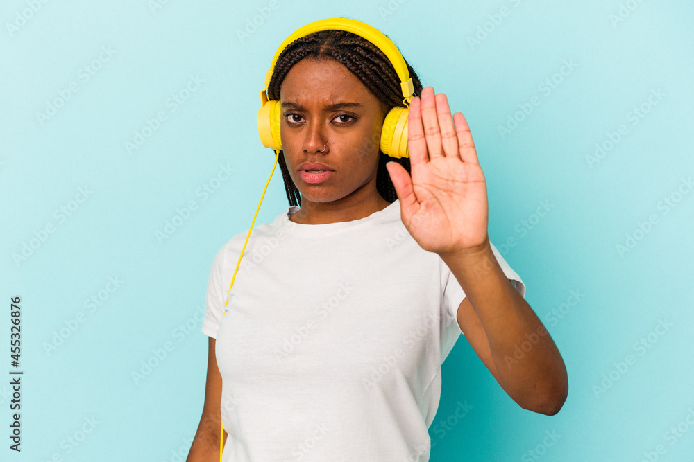 Young African American woman listening to music isolated on blue background  standing with outstretched hand showing stop sign, preventing you.