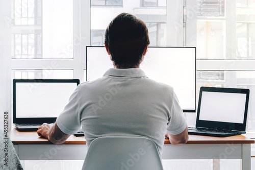 Obraz na plátně Man sitting at workplace with two laptops and monitor near the window