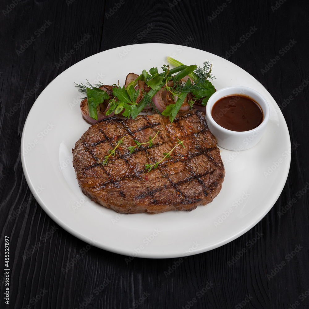 Grilled black angus steak ribeye on white plate on black wooden background Grilled black angus steak ribeye on white plate on black wooden background