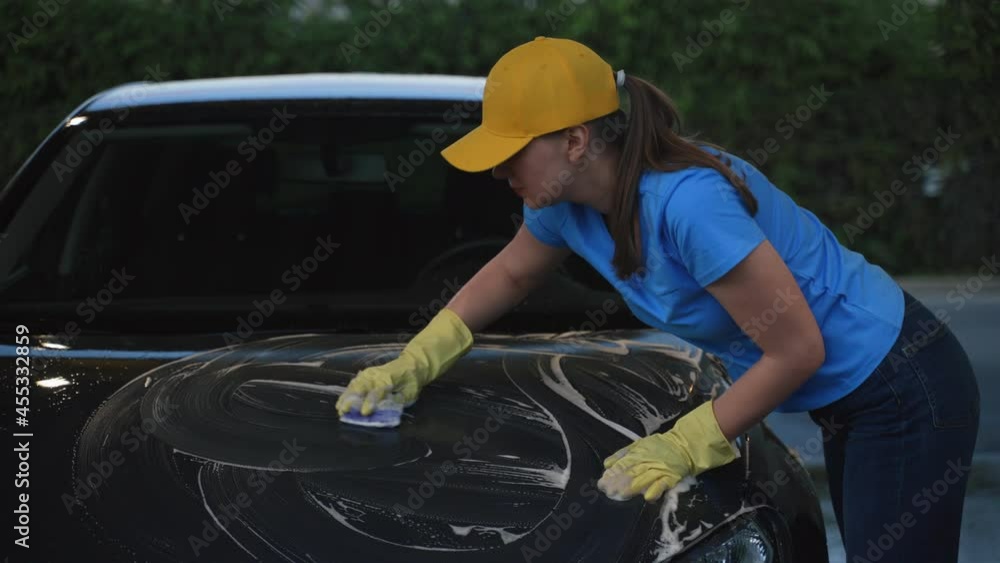 Woman in uniform cleaning car with sponge. Car wash service. Woman in uniform cleaning car with sponge. Car wash service.