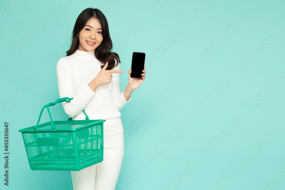 Asian woman smiling and holding grocery basket and presenting mobile phone application isolated on green background, Shopping and Supermarket concept Asian woman smiling and holding grocery basket and presenting mobile phone application isolated on green background, Shopping and Supermarket concept