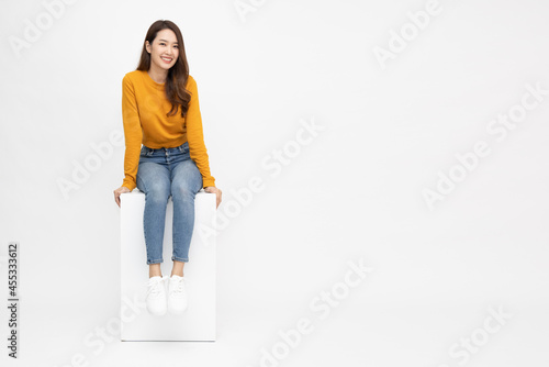 Portrait of young Asian woman sitting on white box isolated over white background, Full body composition