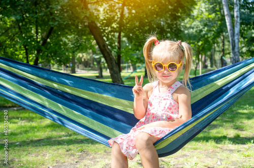 Cute little girl showing with fingers the symbol of victory, while resting on a hammock in the park