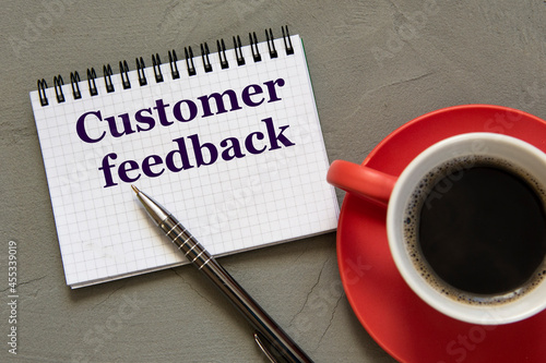 CUSTOMER FEEDBACK - words in a white notebook on a gray background with a pen and a cup of coffee