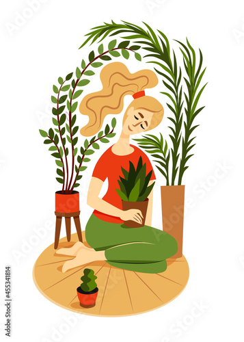 Ð¡ute girl sits on a rug surrounded by house plants and hugs a pot with a indoor flower.