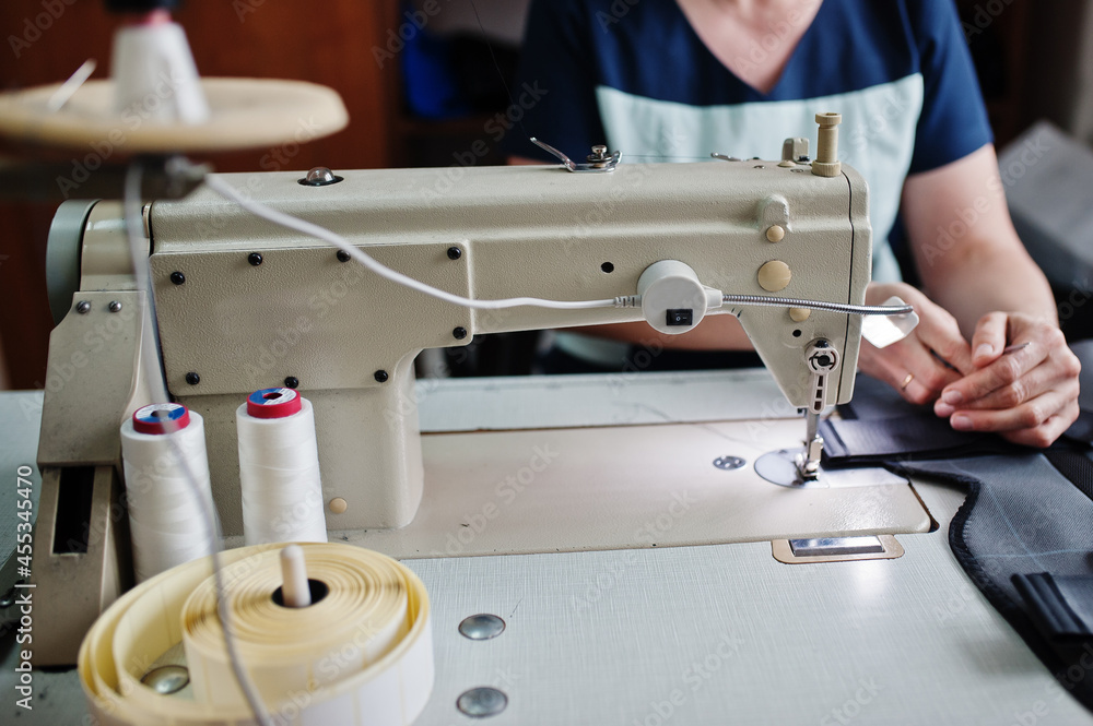 Female hands stitching fabric on professional manufacturing machine at workplace. Sewing process.