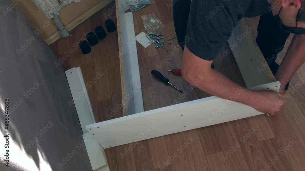 The man connects the pieces of furniture with each other with a confirmation. Collects furniture at home. Other parts are spread out on the floor. Filmed from above The man connects the pieces of furniture with each other with a confirmation. Collects furniture at home. Other parts are spread out on the floor. Filmed from above