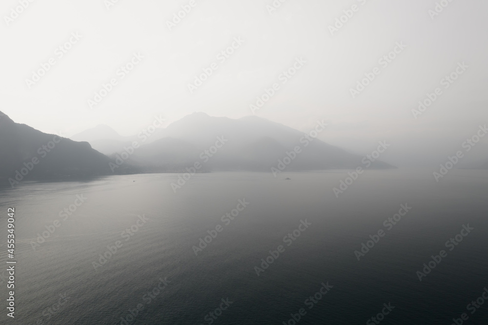 Black and white photo with a foggy mountains in Como lake. Hazy and misty lake view