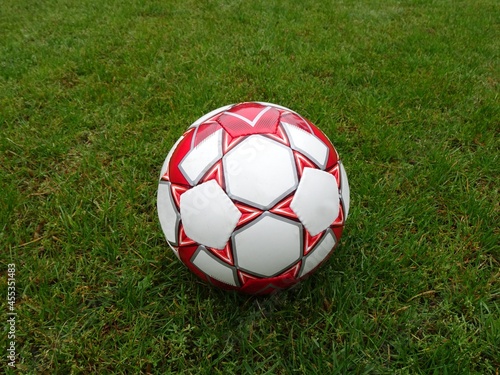 Leather soccer ball in red and white colors on a soccer field.