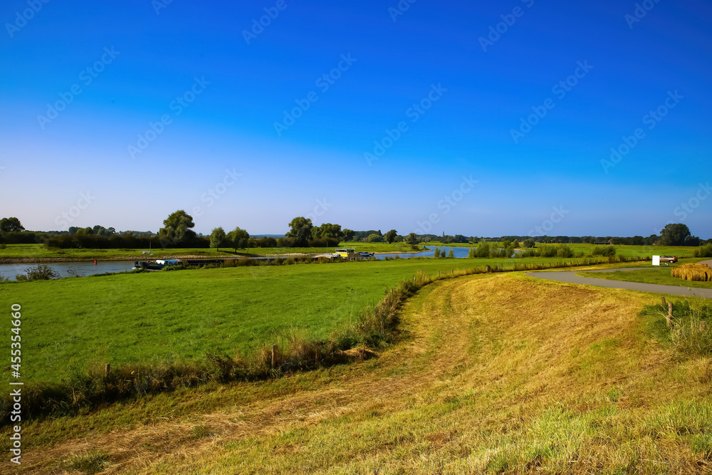View from cycling track on typical dutch rural landscape with agricultural fields and river Ijssel against blue summer sky - between Bronkhorst and Zutphen, Netherlands View from cycling track on typical dutch rural landscape with agricultural fields and river Ijssel against blue summer sky - between Bronkhorst and Zutphen, Netherlands
