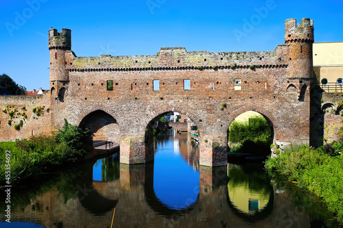 View over water canal on medieval watergate stone wall with 3 arches from 14th century with reflection against blue summer sky - Zutphen (Berkelpoort), Netherlands photo