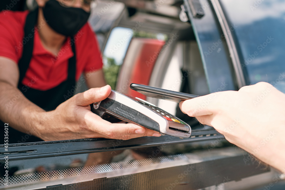 Seller of takeout food holding payment terminal in window of truck while client paying for snack Seller of takeout food holding payment terminal in window of truck while client paying for snack