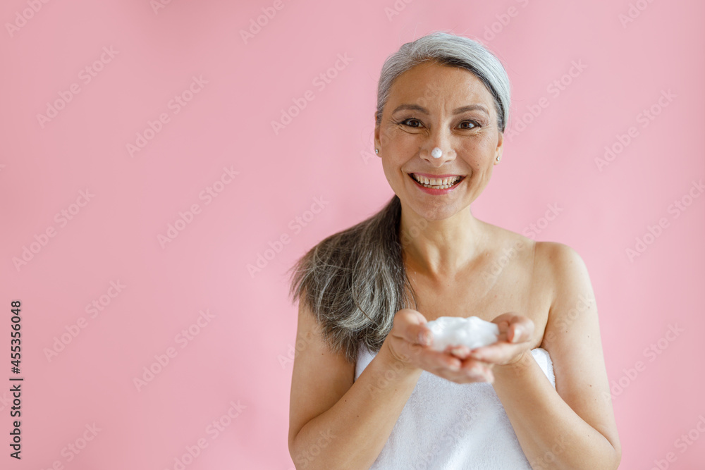 Jouful silver haired middle aged Asian lady with handful of foam stands on pink background in studio, space for text. Mature beauty lifestyle Jouful silver haired middle aged Asian lady with handful of foam stands on pink background in studio, space for text. Mature beauty lifestyle
