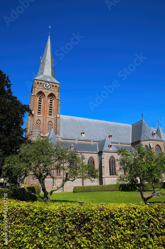 View on dutch neo gothic church from 18th century with green trees against blue summer sky - Baak, Sint Martinuskerk, Netherlands photo