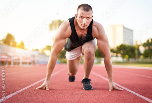 Young millennial determined muscular sportsman starting running on a red running court in a stadium - Athletic motivated runner preparing for running race and looking forward into the distance