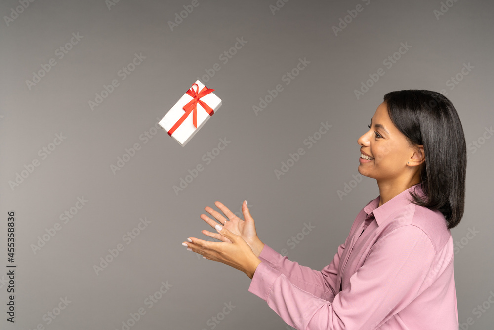 Happy excited woman throwing up gift box over gray wall background. Low price for presents on holiday season, sales and discount and black friday concept. Female cheering for seasonal special offers Happy excited woman throwing up gift box over gray wall background. Low price for presents on holiday season, sales and discount and black friday concept. Female cheering for seasonal special offers
