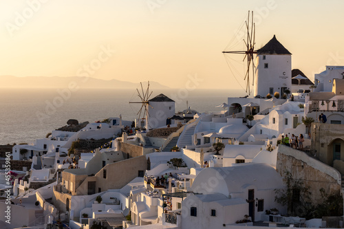  Whitewashed houses and windmills in Oia in warm rays of sunset on Santorini island. Greece