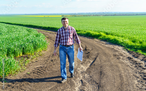 a man as a farmer poses in a field  dressed in a plaid shirt and jeans  checks reports and inspects young sprouts crops of wheat  barley or rye  or other cereals  a concept of agriculture and agronomy