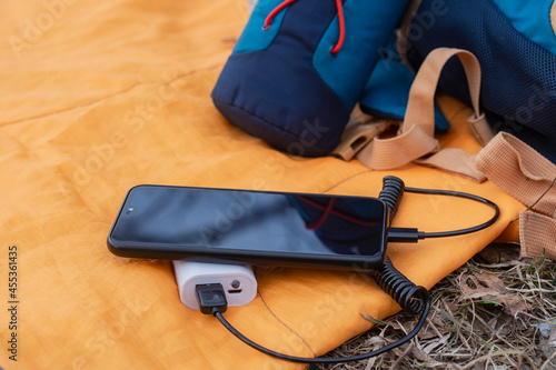 The smartphone is being charged with a portable charger. Power bank with a mobile phone on a sleeping bag with a backpack.