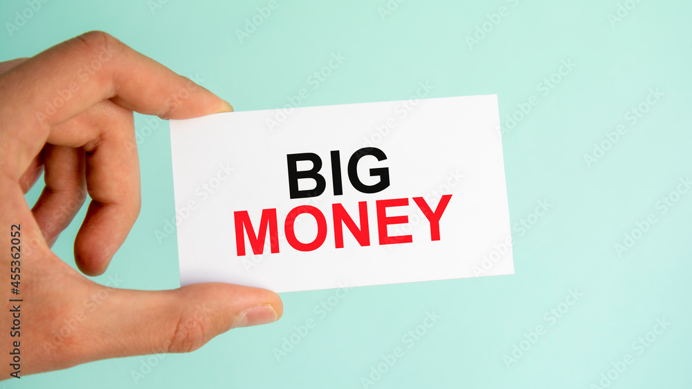businessman's hand holding paper business card with text Big Money, closeup light blue background businessman's hand holding paper business card with text Big Money, closeup light blue background