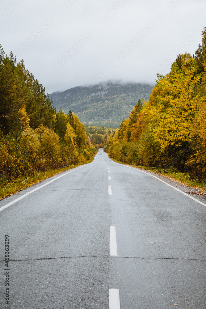 Autumn the road goes into the distance. An empty road passes through the forest. Asphalt in the mountains against the background of the autumn forest. Autumn the road goes into the distance. An empty road passes through the forest. Asphalt in the mountains against the background of the autumn forest.