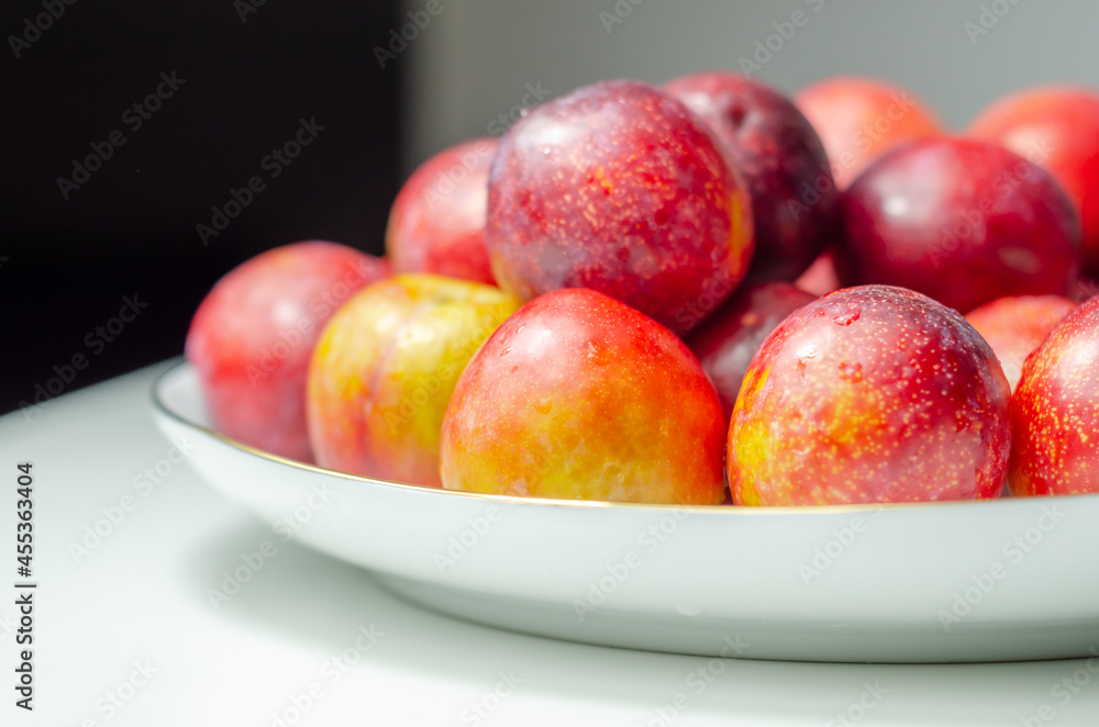 Closeup on fresh and ripe plums on a white ceramic plate Closeup on fresh and ripe plums on a white ceramic plate