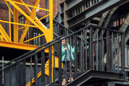 Little caucasian blonde girl in fashionable clothes descends the metal steps