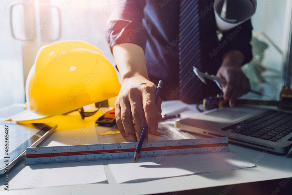 Two colleagues discussing data working and tablet, laptop with on on architectural project at construction site at desk in office Two colleagues discussing data working and tablet, laptop with on on architectural project at construction site at desk in office