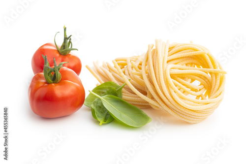 Italian pasta nest, tomato and basil leaves. Uncooked spaghetti nest