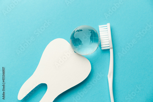 The concept of the International Day of the Dentist. White toothbrush, paper tooth and glass globe on a blue background. Top view. Flat lay. Close-up. Copy space