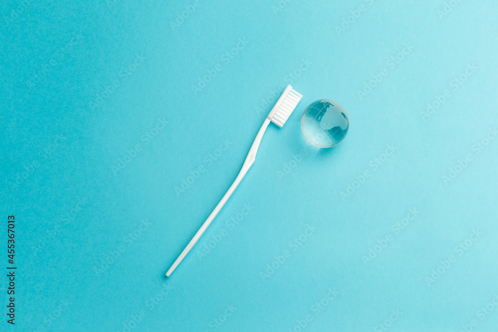 The concept of the International Day of the Dentist. White toothbrush and glass globe on a blue background. Top view. Flat lay. Close-up. Copy space