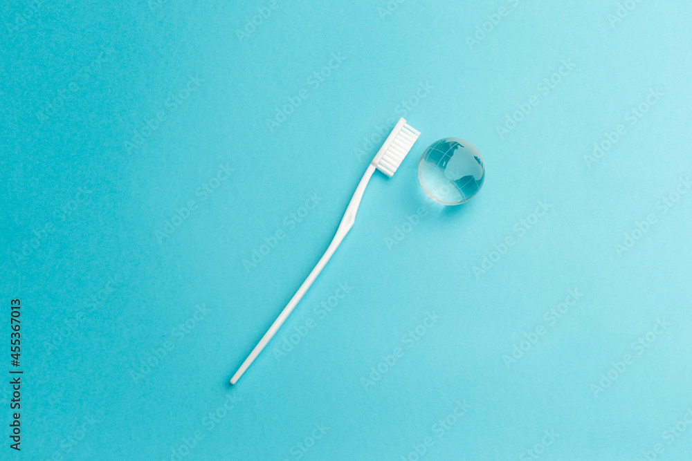 The concept of the International Day of the Dentist. White toothbrush and glass globe on a blue background. Top view. Flat lay. Close-up. Copy space The concept of the International Day of the Dentist. White toothbrush and glass globe on a blue background. Top view. Flat lay. Close-up. Copy space