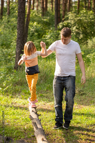 Caucasian girl of 6 years old walking on a log holding dad's hand.